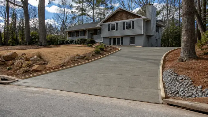 A broom drags across a driveway creating a slip-resistant texture. at a grey split-level home in Sandy Springs, GA, under broken cloud.