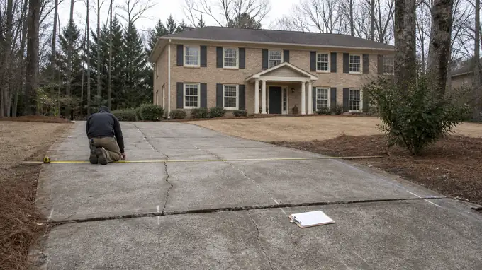 Existing driveway measured and marked before it is replaced at a tan-brick colonial in Sandy Springs, GA, under an overcast sky.