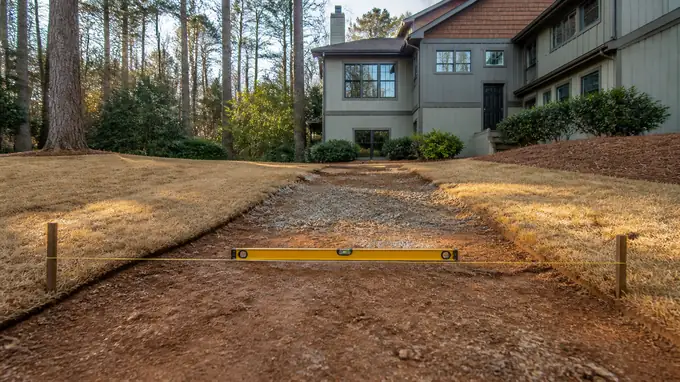 Backyard grade checked with a level and string before a patio pour at a grey split-level home in Sandy Springs, GA, in early morning light.