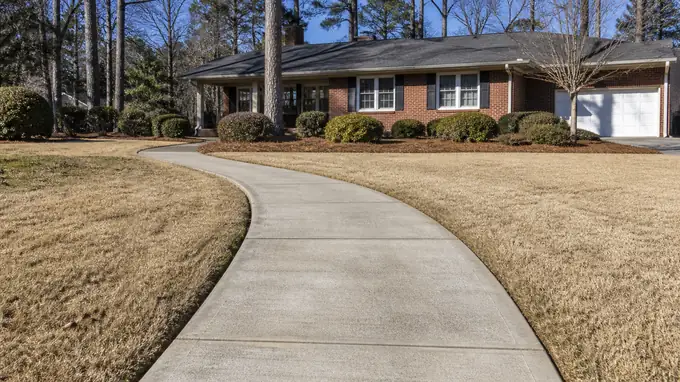 Curving concrete walkway crossing a front yard at a red-brick ranch home in Sandy Springs, GA, in clear late-morning sun.
